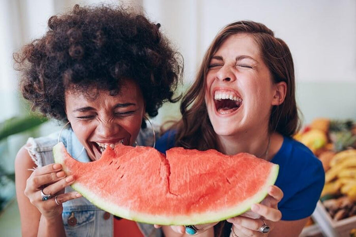 two women laugh while sharing a watermelon